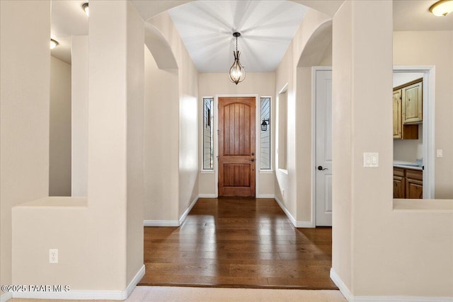 foyer featuring arched walkways, baseboards, and wood finished floors