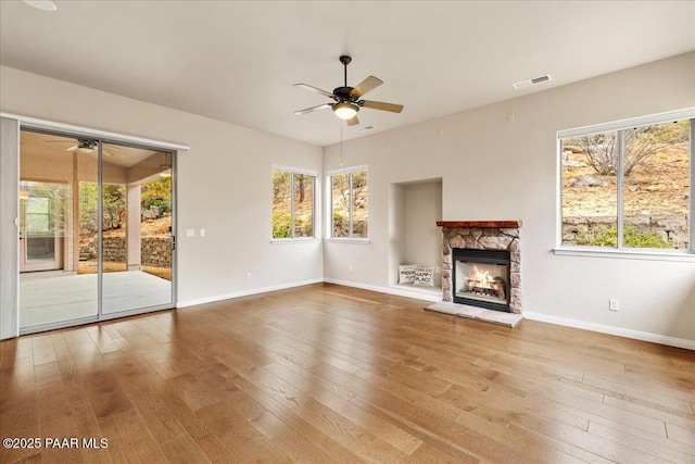 unfurnished living room with a stone fireplace, hardwood / wood-style flooring, visible vents, and ceiling fan