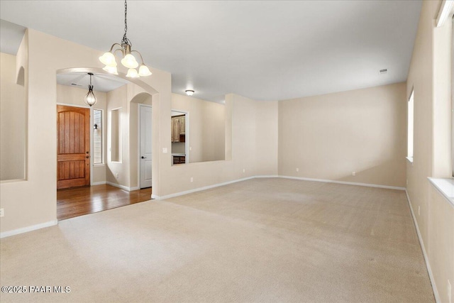 empty room with baseboards, carpet floors, arched walkways, and a chandelier