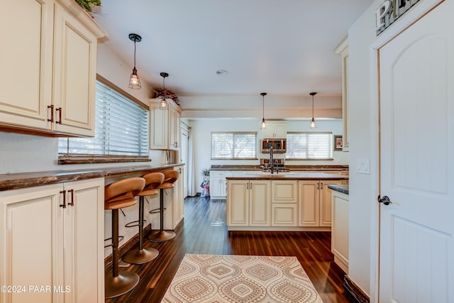 kitchen with decorative light fixtures, dark wood-type flooring, and cream cabinets