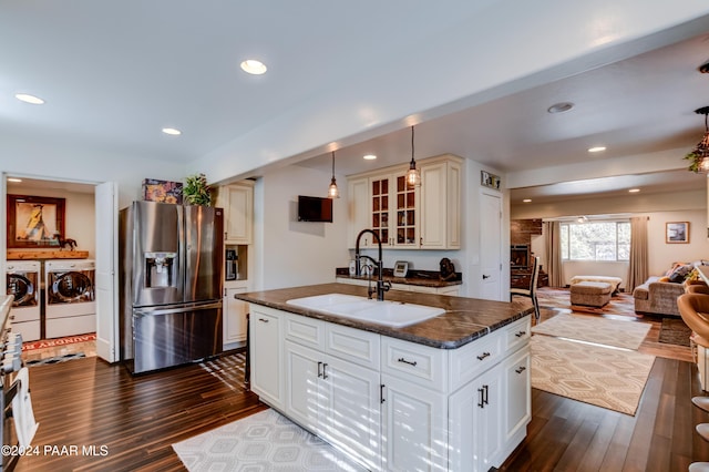 kitchen featuring a kitchen island with sink, sink, washer and dryer, decorative light fixtures, and stainless steel fridge with ice dispenser