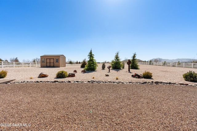 view of yard featuring a rural view, an outbuilding, fence, a shed, and a mountain view