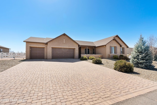 ranch-style house with decorative driveway, an attached garage, fence, and stucco siding