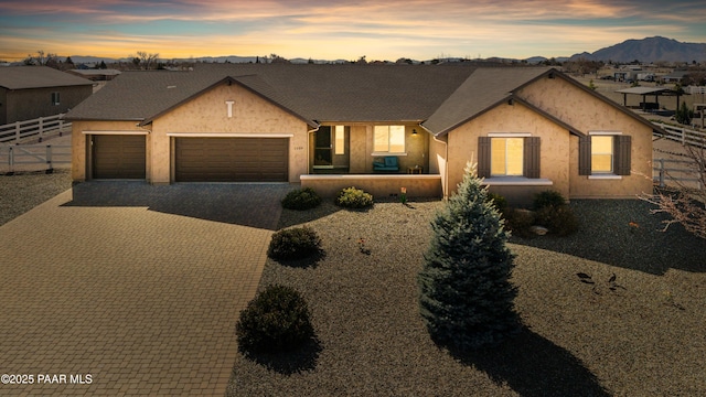 view of front of property featuring decorative driveway, stucco siding, an attached garage, a mountain view, and fence