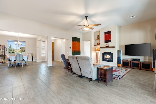 living room with a warm lit fireplace, baseboards, visible vents, and ceiling fan with notable chandelier