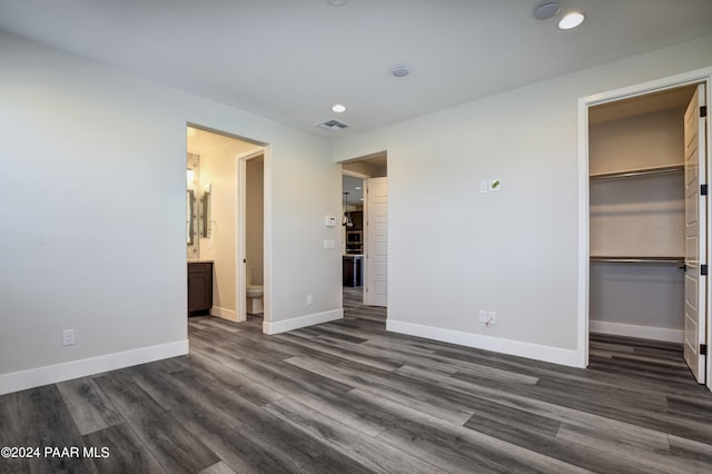 unfurnished bedroom with ensuite bath, a spacious closet, and dark wood-type flooring