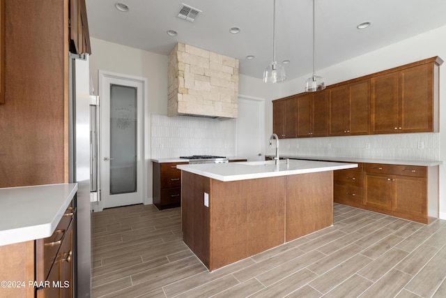 kitchen featuring sink, a center island with sink, pendant lighting, and light hardwood / wood-style flooring