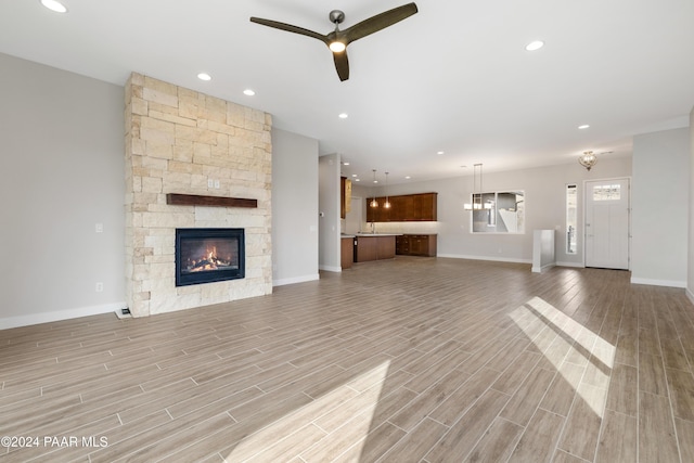 unfurnished living room with light wood-type flooring, a stone fireplace, ceiling fan, and sink