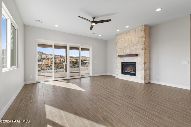 unfurnished living room with a stone fireplace, ceiling fan, and dark wood-type flooring