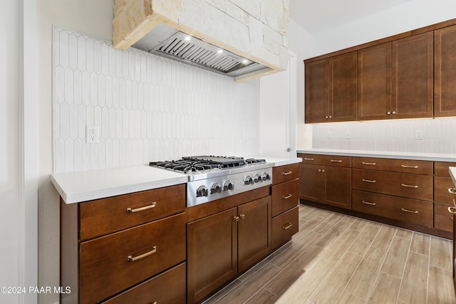 kitchen featuring backsplash, premium range hood, light hardwood / wood-style floors, dark brown cabinetry, and stainless steel gas cooktop