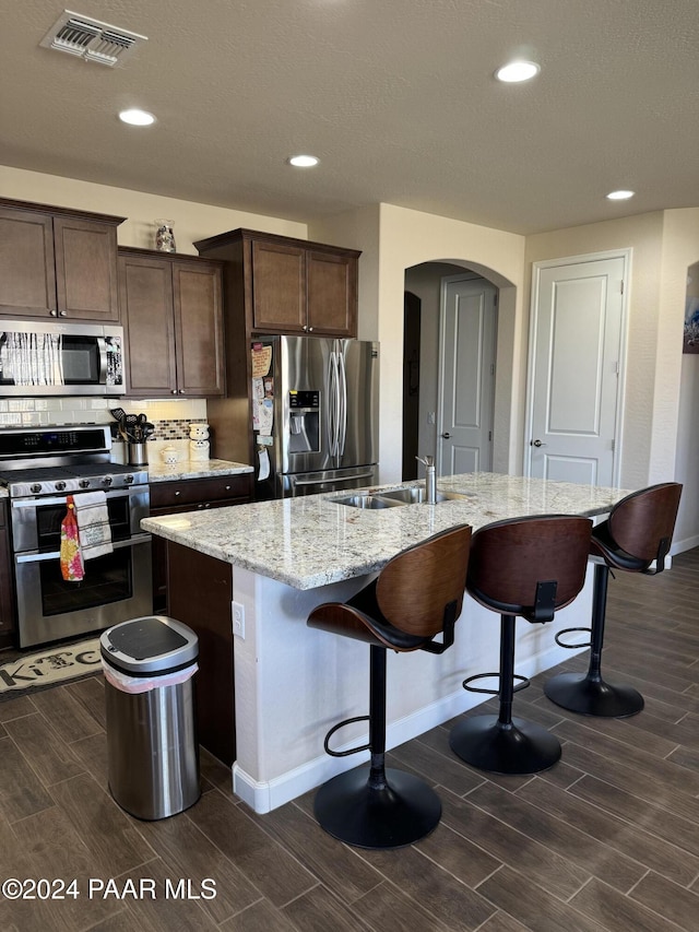 kitchen with decorative backsplash, appliances with stainless steel finishes, sink, and an island with sink