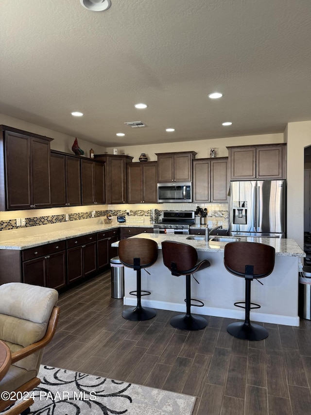 kitchen with a kitchen island with sink, dark brown cabinetry, stainless steel appliances, and a breakfast bar area