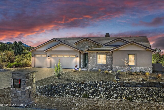 view of front of property featuring stucco siding, stone siding, a tiled roof, a garage, and a chimney