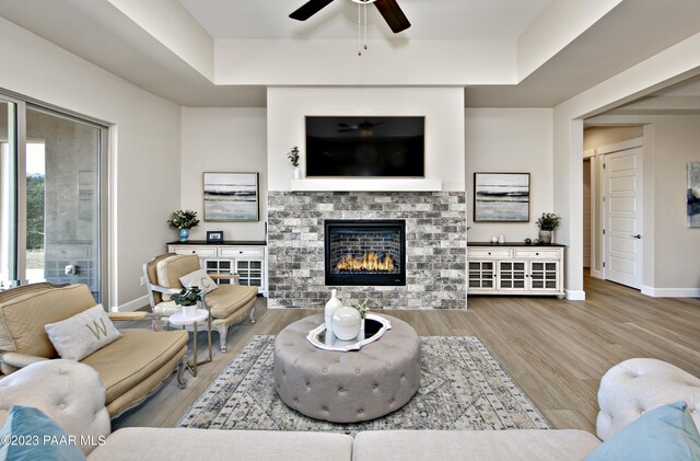 living room featuring baseboards, wood finished floors, a glass covered fireplace, and a ceiling fan