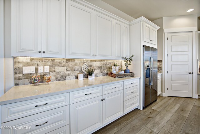 kitchen featuring light wood-type flooring, stainless steel fridge with ice dispenser, backsplash, light stone counters, and white cabinets