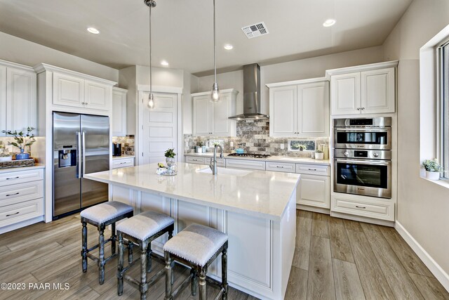 kitchen with visible vents, light wood-style flooring, appliances with stainless steel finishes, a sink, and wall chimney range hood