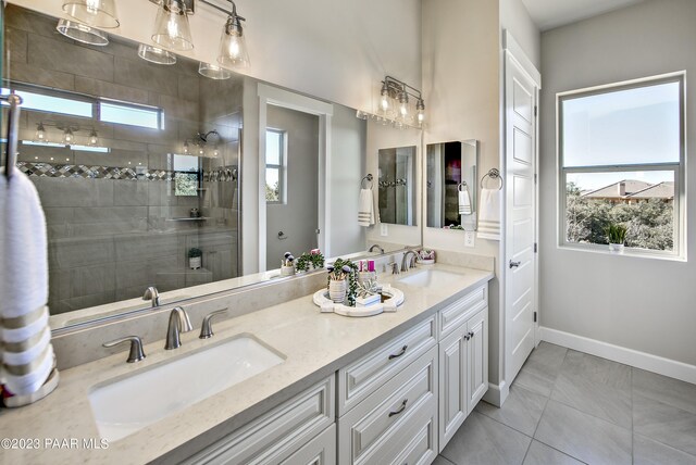 full bathroom with double vanity, a tile shower, baseboards, and a sink