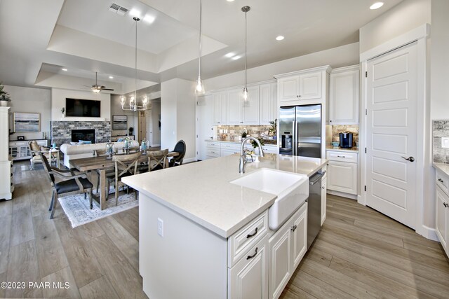 kitchen with a tray ceiling, a sink, a ceiling fan, appliances with stainless steel finishes, and light wood-style floors
