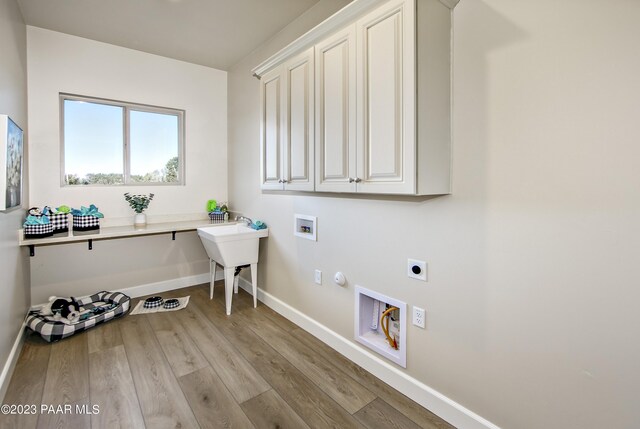 clothes washing area with hookup for an electric dryer, hookup for a washing machine, gas dryer hookup, light wood finished floors, and cabinet space