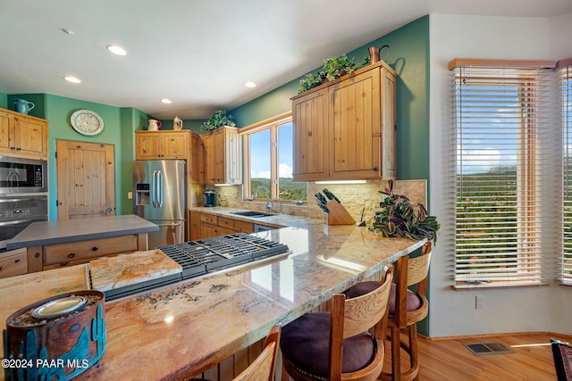 kitchen featuring sink, light hardwood / wood-style floors, a breakfast bar area, decorative backsplash, and appliances with stainless steel finishes