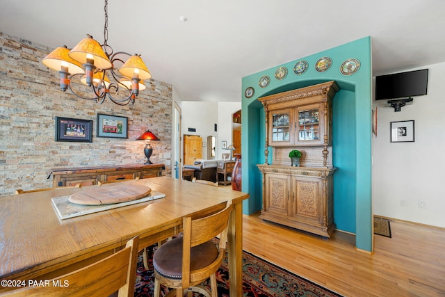 dining area with an inviting chandelier, light hardwood / wood-style flooring, and brick wall