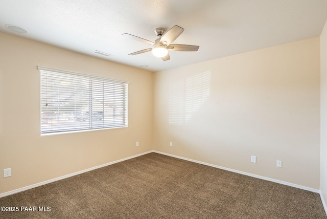 spare room featuring dark colored carpet, visible vents, baseboards, and a ceiling fan