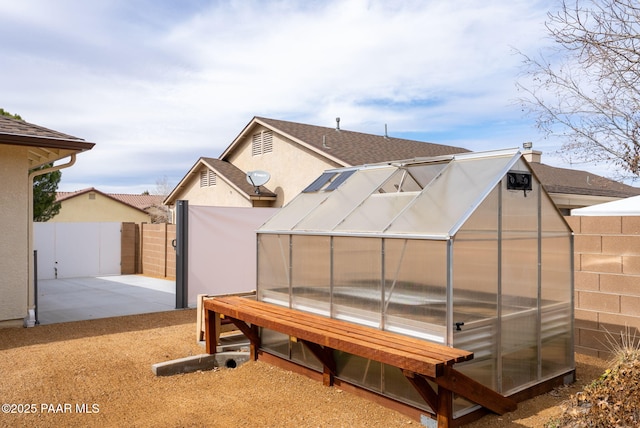 exterior space with stucco siding, a patio, fence, a greenhouse, and an outdoor structure