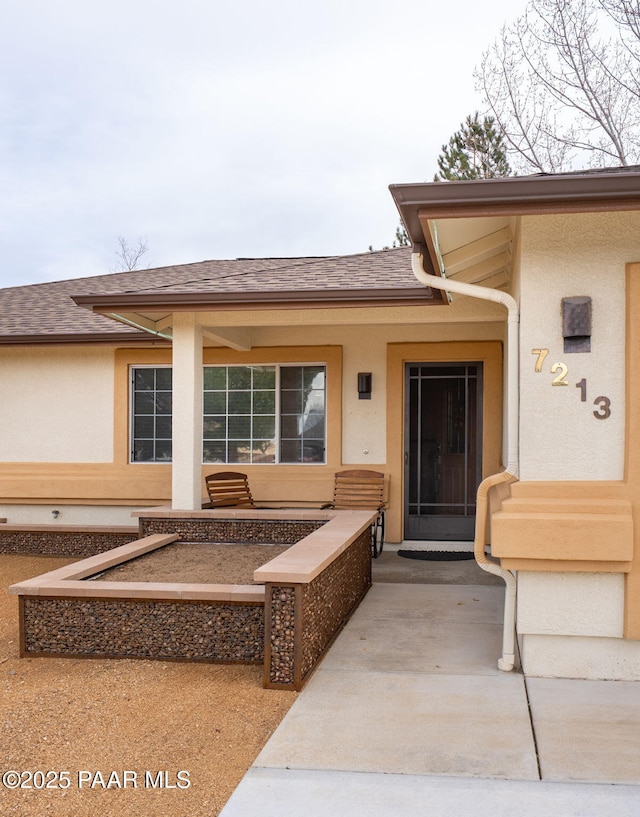 entrance to property with stucco siding and roof with shingles