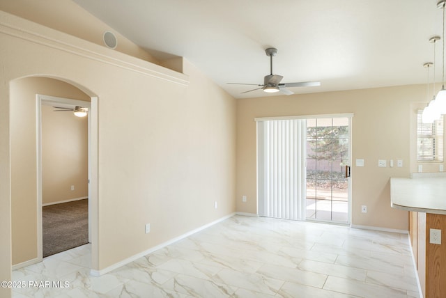 empty room featuring baseboards, vaulted ceiling, arched walkways, marble finish floor, and a ceiling fan