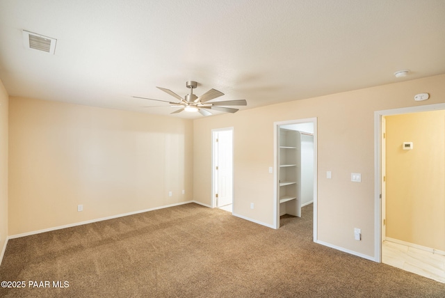 unfurnished bedroom featuring visible vents, a walk in closet, ceiling fan, baseboards, and carpet