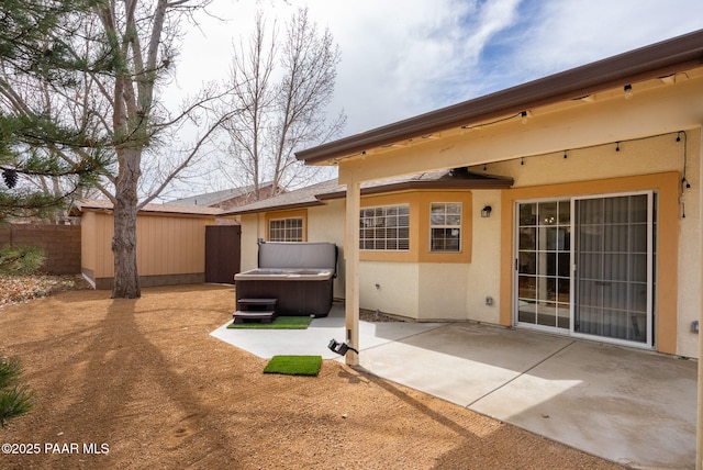 rear view of house featuring stucco siding, a patio, fence, and a hot tub