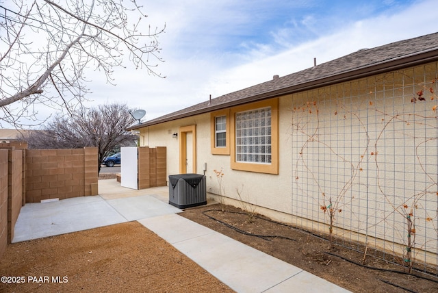 view of home's exterior featuring a patio area, fence, roof with shingles, and stucco siding