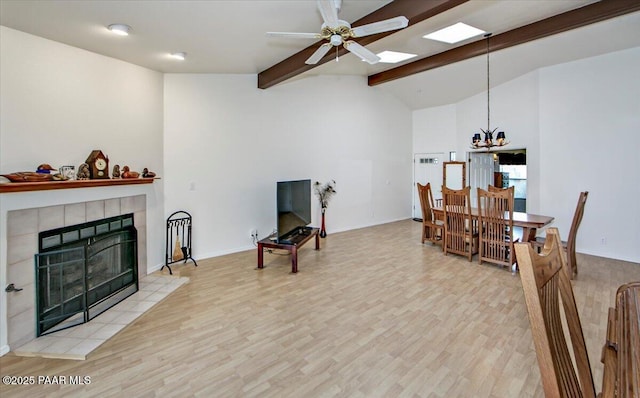 living room featuring wood finished floors, baseboards, vaulted ceiling with beams, a tiled fireplace, and ceiling fan with notable chandelier