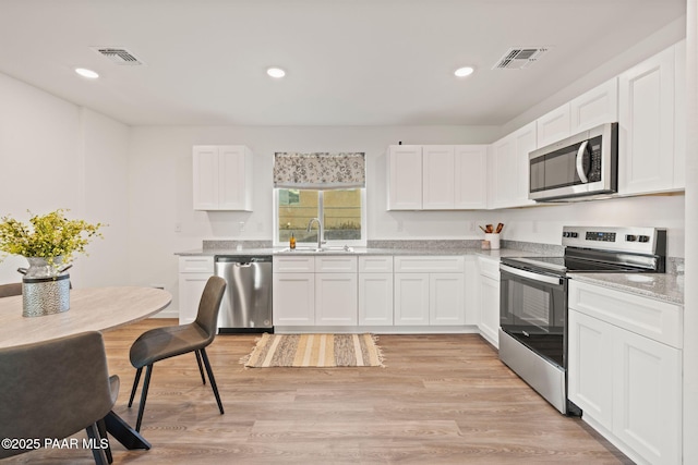 kitchen with light wood-type flooring, stainless steel appliances, white cabinetry, and sink