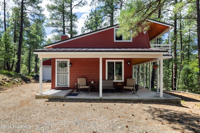 back of house featuring metal roof, a patio, a chimney, and a standing seam roof
