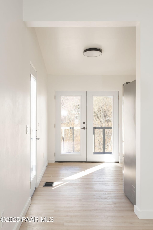 doorway with vaulted ceiling with beams, plenty of natural light, french doors, and light wood-type flooring