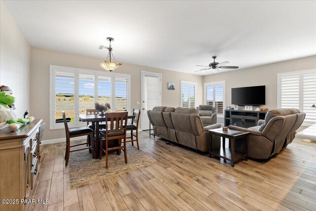 living room featuring baseboards, a ceiling fan, visible vents, and light wood-type flooring