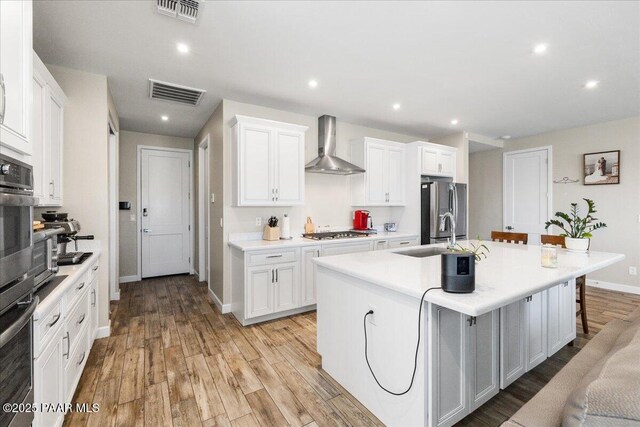 kitchen with wall chimney exhaust hood, a kitchen island with sink, visible vents, and appliances with stainless steel finishes