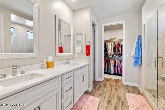 bathroom featuring wood finished floors, a sink, a shower stall, and double vanity