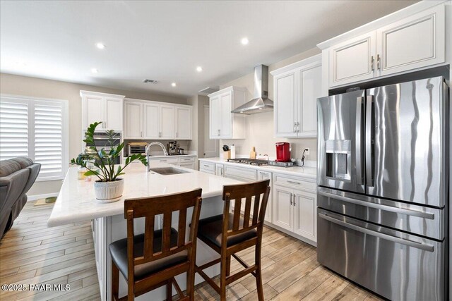 kitchen featuring light countertops, wall chimney range hood, a sink, appliances with stainless steel finishes, and white cabinetry