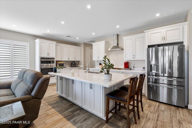 kitchen with stainless steel appliances, light wood finished floors, light countertops, wall chimney exhaust hood, and white cabinetry