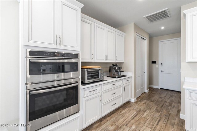 kitchen featuring stainless steel double oven, light wood-type flooring, a toaster, light countertops, and visible vents