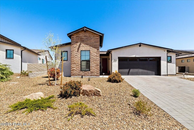 view of front of property featuring stone siding, stucco siding, decorative driveway, and a garage