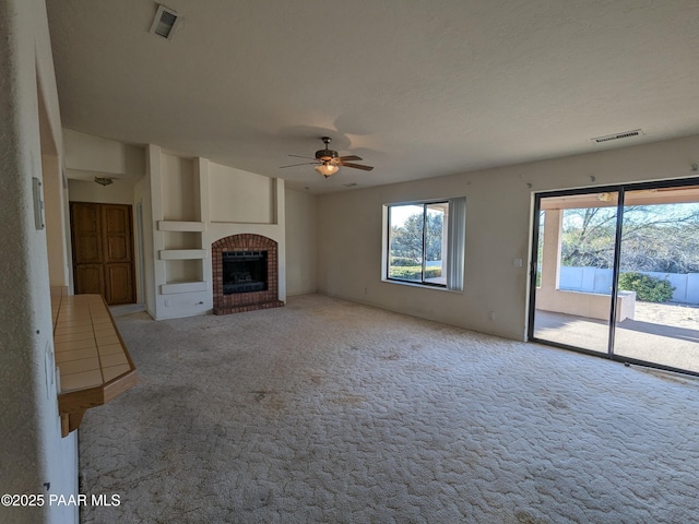 unfurnished living room with ceiling fan, a fireplace, carpet flooring, and visible vents