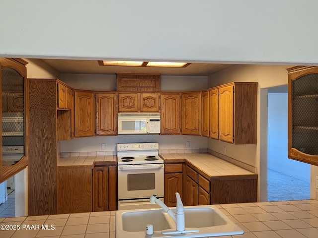kitchen with a sink, brown cabinetry, tile countertops, and white appliances
