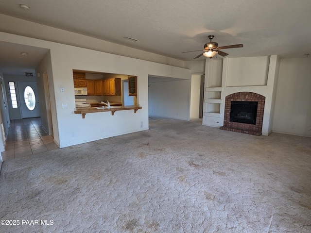 unfurnished living room featuring a ceiling fan, light colored carpet, a brick fireplace, a sink, and baseboards