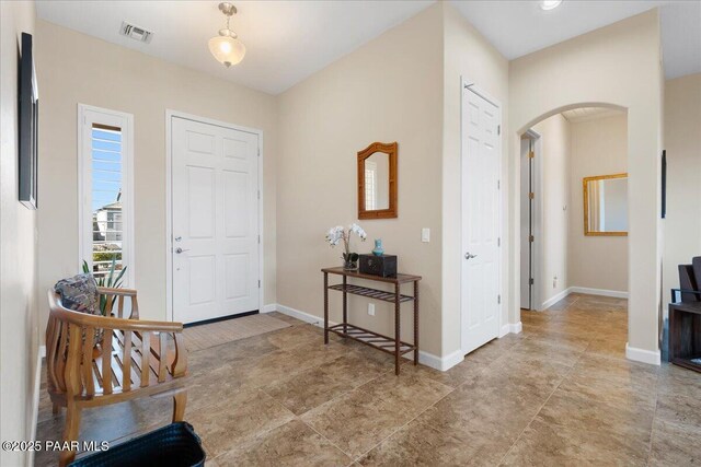 foyer entrance featuring arched walkways, visible vents, and baseboards