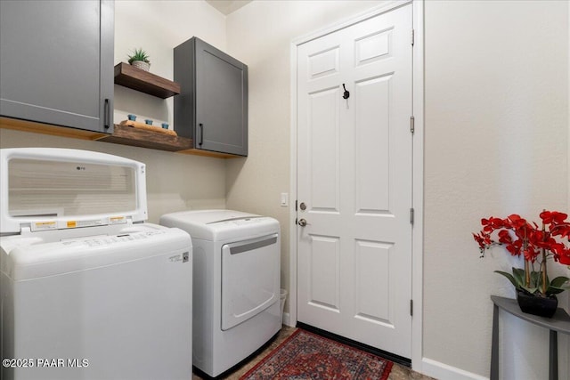 clothes washing area featuring washing machine and dryer, cabinet space, and baseboards