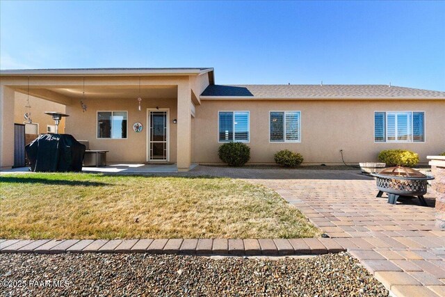 rear view of property featuring an outdoor fire pit, stucco siding, a lawn, and a patio
