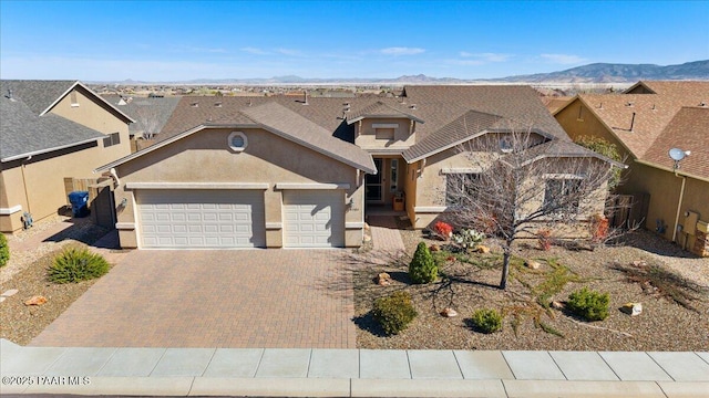 view of front facade with stucco siding, decorative driveway, an attached garage, and a mountain view